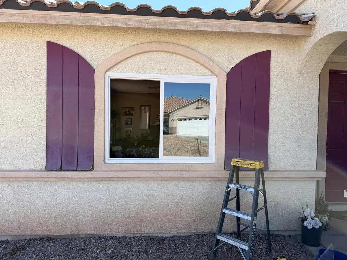 Sliding window set into an arched opening flanked by shutters.