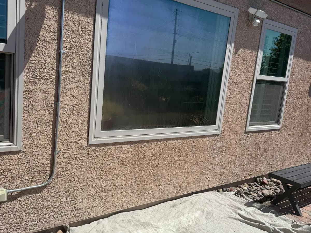 Large picture window on tan stucco above a paver patio.