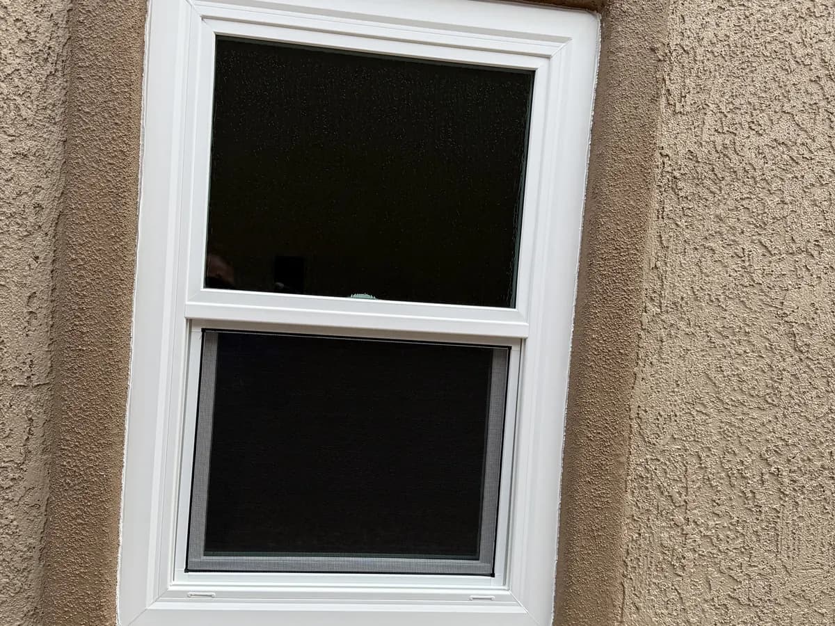 Single-hung window with screen in tan stucco.