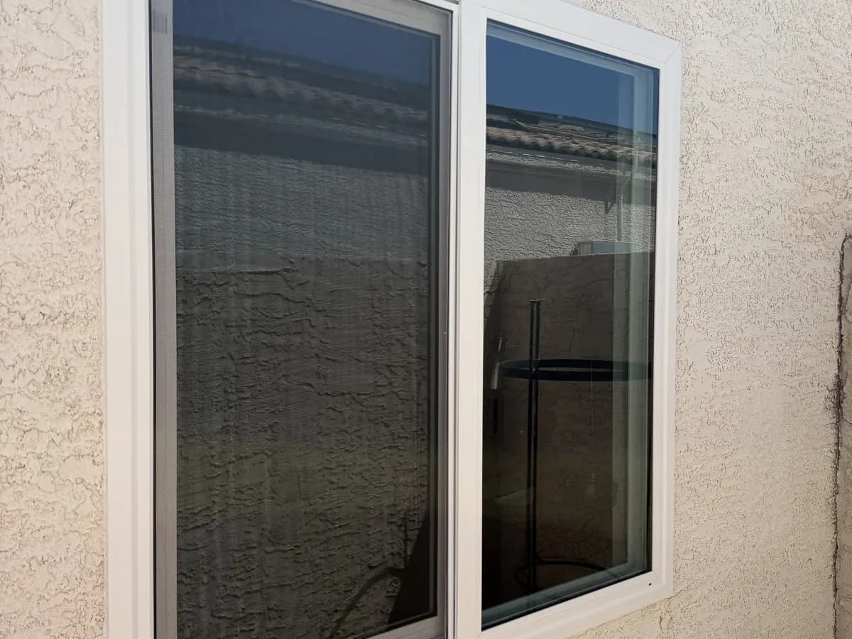 Two-panel white sliding window in cream stucco under a tile roof.