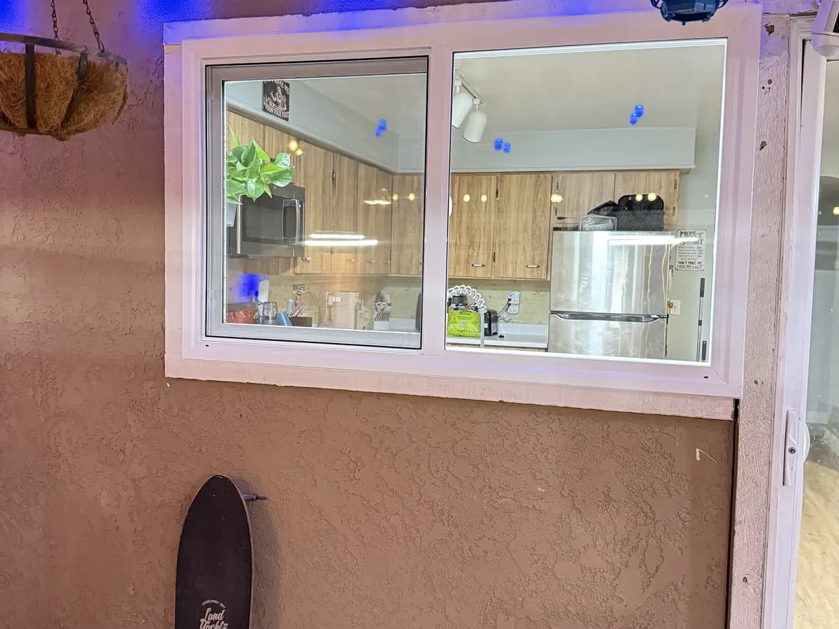 Sliding window looking into a kitchen from a covered patio at dusk.